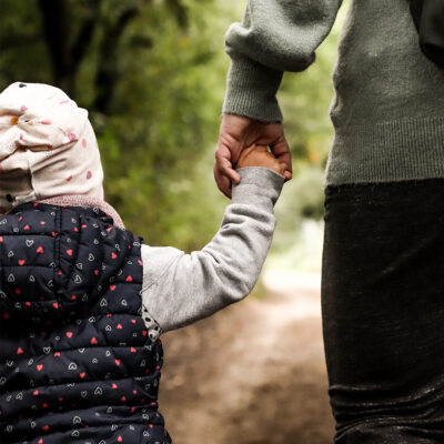 Mutter und Tochter spazieren Hand in Hand durch den Wald.