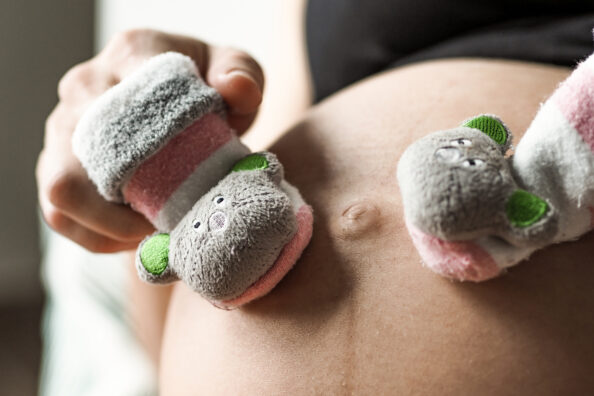 Schwangere Frau streichelt mit Rasselsöckchen über ihren Babybauch.