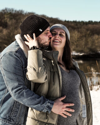 Mann hält Babybauch seiner Freundin und küsst sie.