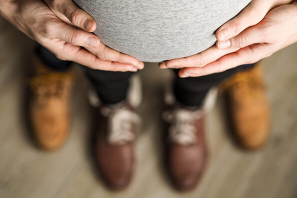 Babybauch von oben mit Händen, die den Bauch umfassen.