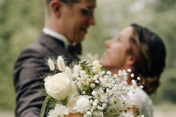 Ein frisch verheiratetes Paar hält den Brautstrauß in die Kamera und blickt sich glücklich in die Augen.